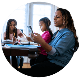 Mother sitting at kitchen table looking at kid's grades on mobile device