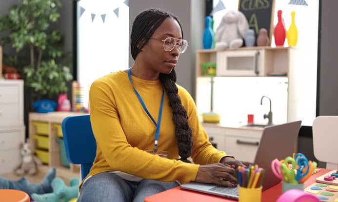 Young teacher working on a laptop in a classroom at a deck featuring one of PowerSchool’s cloud bundles
